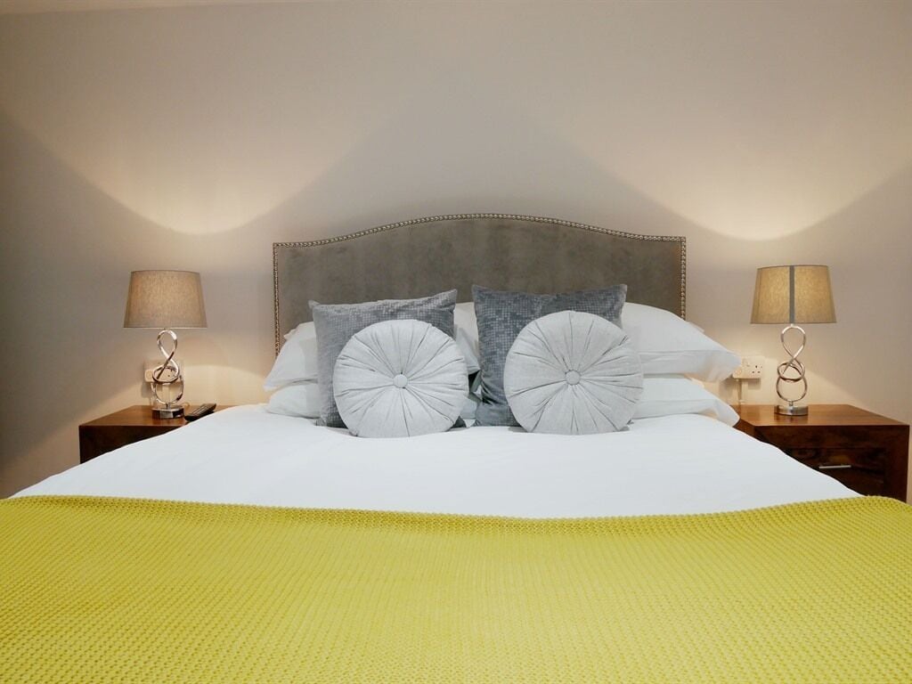 A neatly made bed with a grey headboard, two bedside lamps, and a yellow blanket.