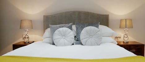 A neatly made bed with a grey headboard, two bedside lamps, and a yellow blanket.
