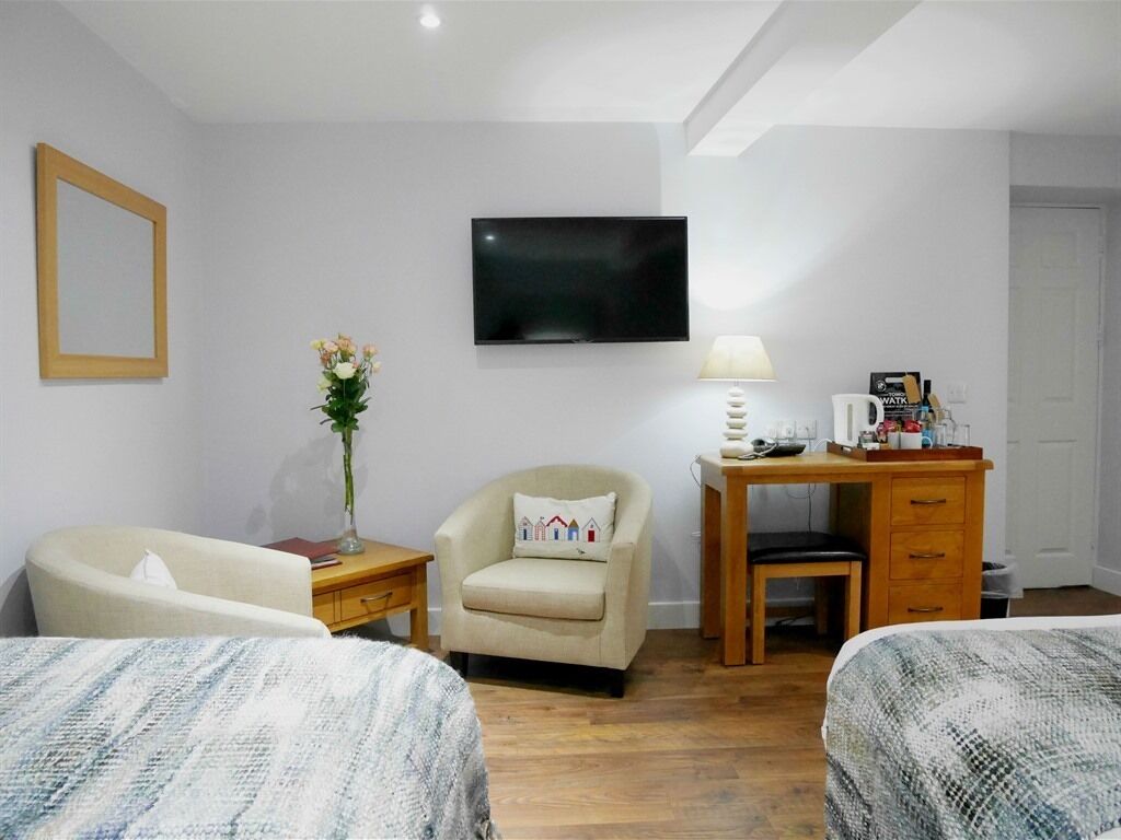 Ett hotellrum med två sängar, ett skrivbord med en lampa, en stol, en tv och ett litet bord med en kaffebryggare.