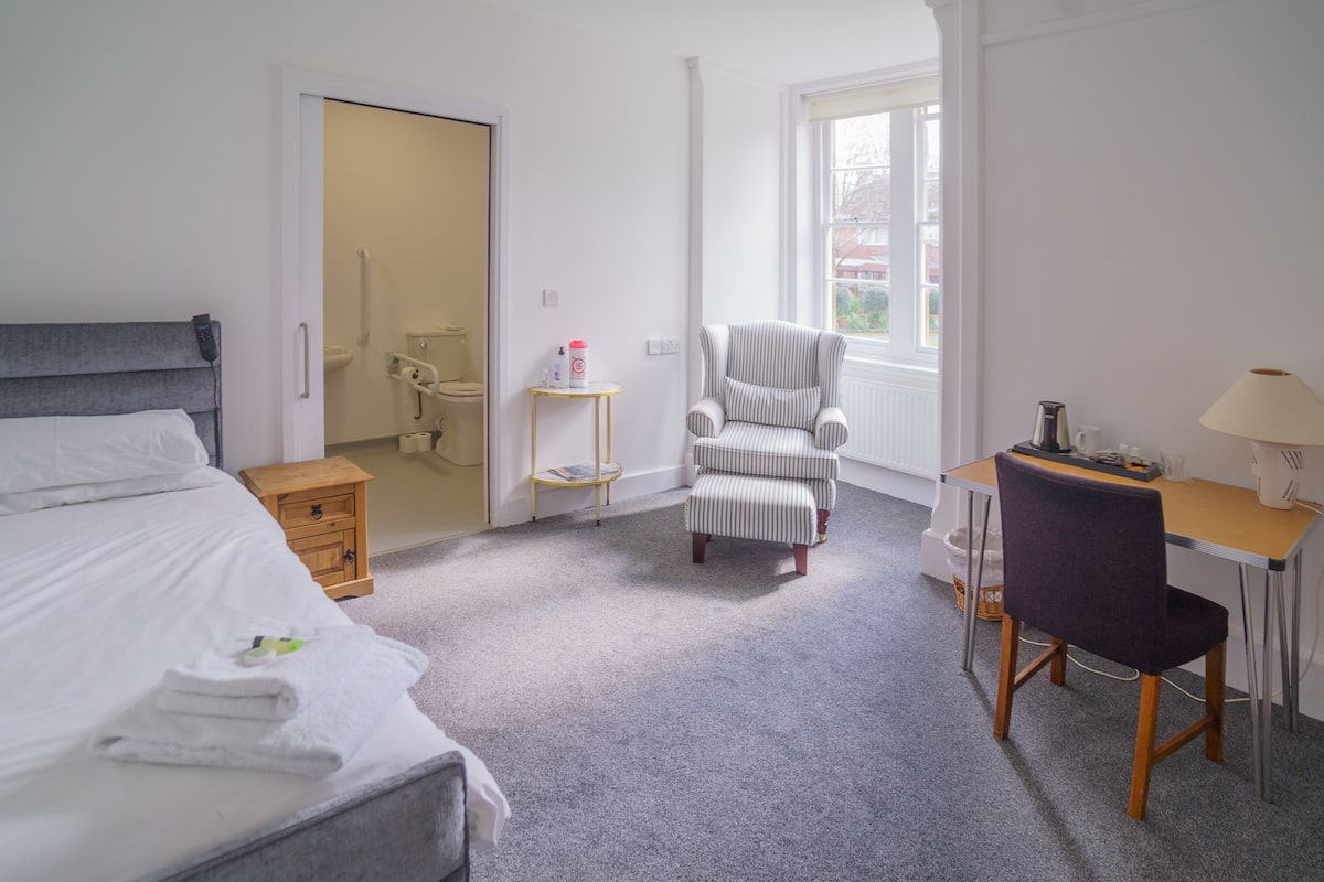 Hotellihuone, jossa on sänky, työpöytä, tuoli, pieni pöytä ja ikkuna.