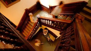 Un escalier en bois avec une rampe et une personne assise sur un banc, en bas.