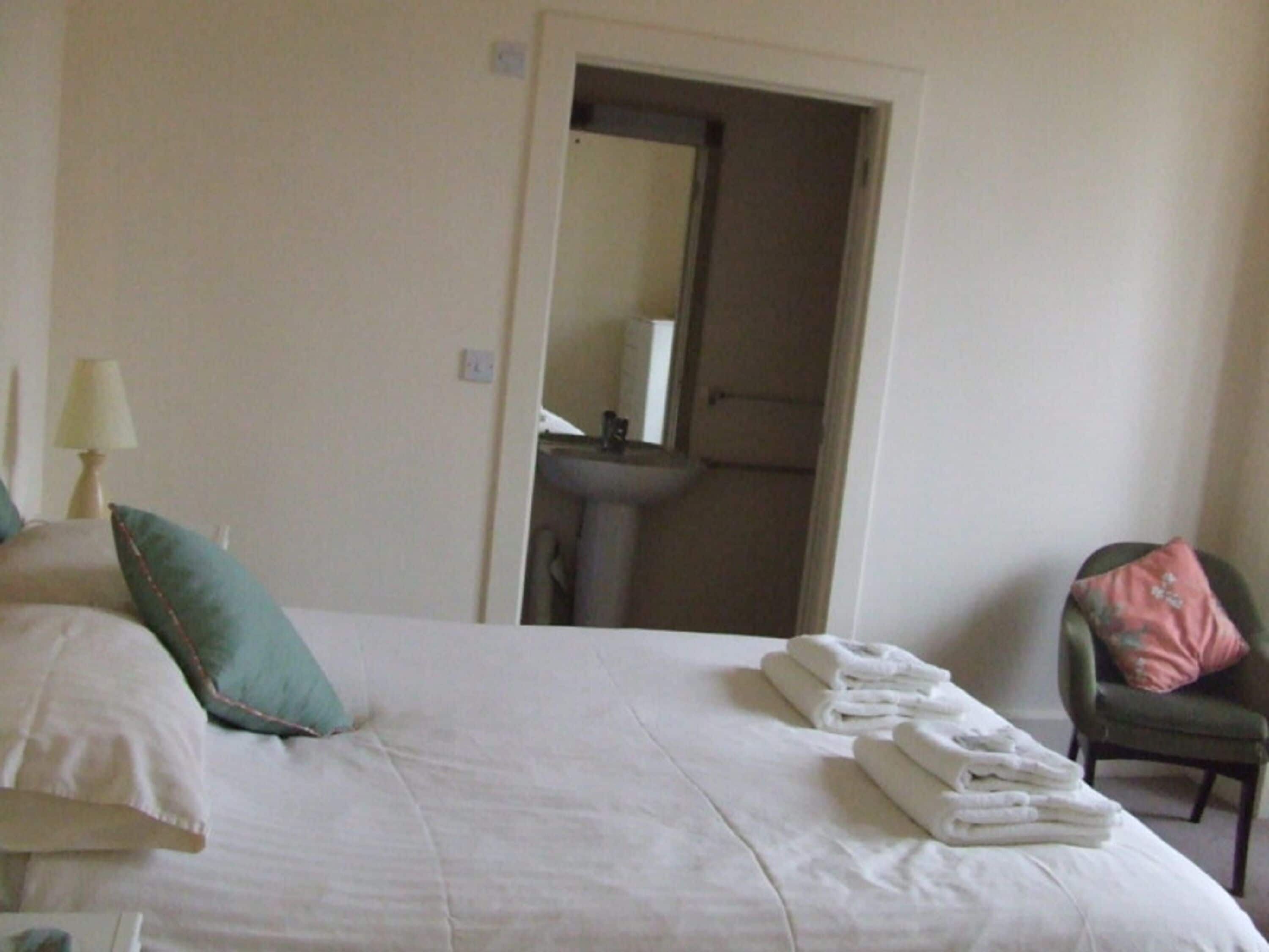 Een hotelkamer met een bed, een stoel, een lamp en een zichtbare badkamer door een geopende deur.
