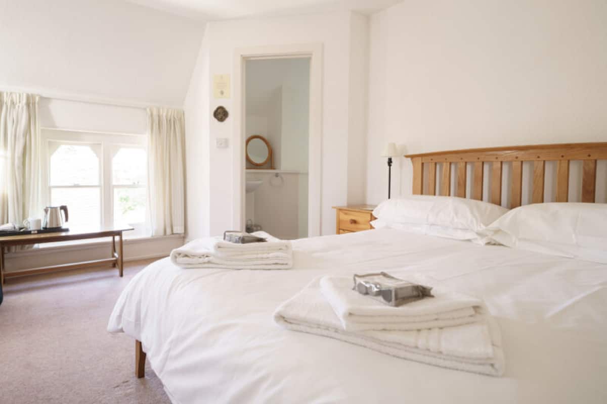 Hotellihuone, jossa on suuri sänky, yöpöytä, peili ja ikkuna, jossa on verhot.