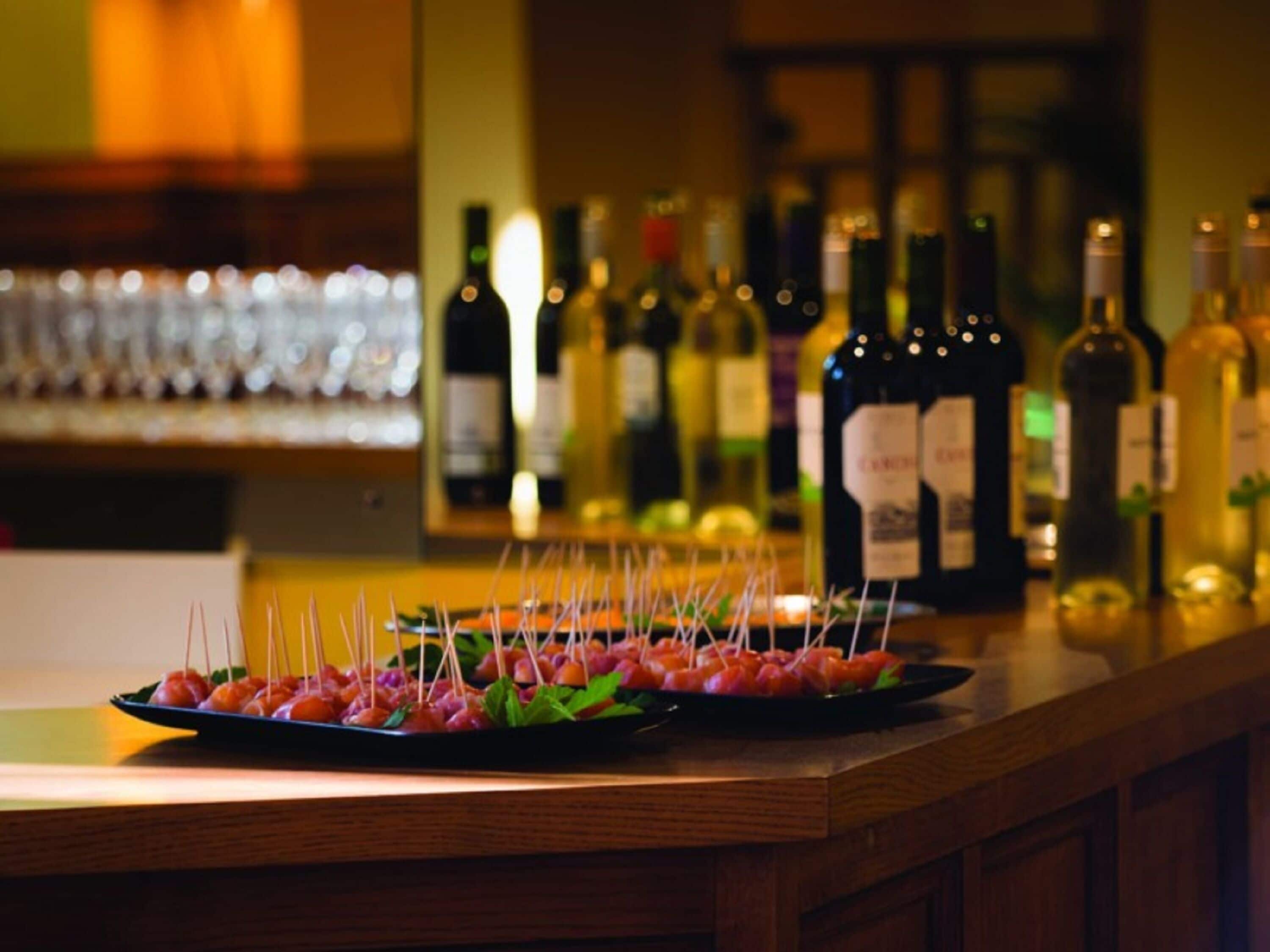 A bar area with a tray of skewered appetizers and a selection of wine bottles in the background.
