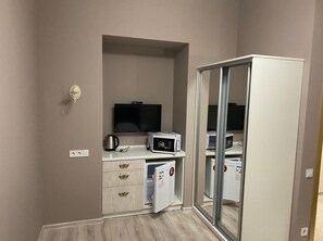 Eine kompakte Küchenzeile mit Mikrowelle, Toaster und Wasserkocher, einem flachbildfernseher an der Wand und einem Kühlschrank mit Schiebetür.