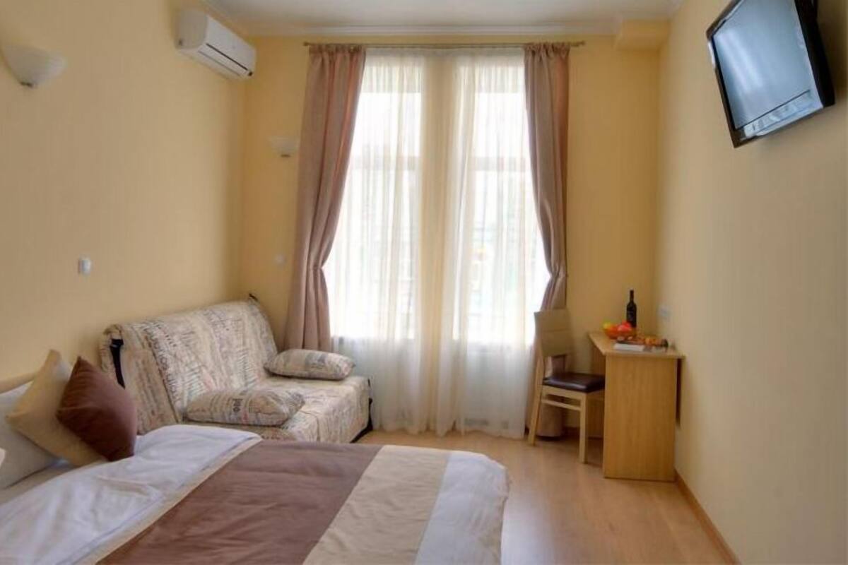 Una habitación de hotel con una cama, un sofá, un escritorio y un televisor fijado a la pared.