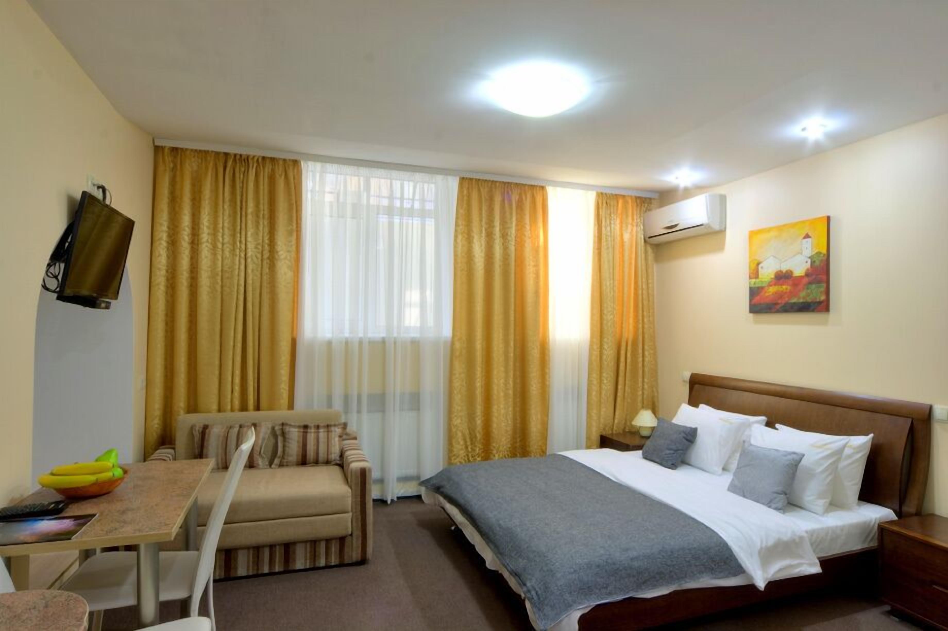 A hotel room with a bed, a sofa, a small table with a bowl of fruit, and a painting on the wall.