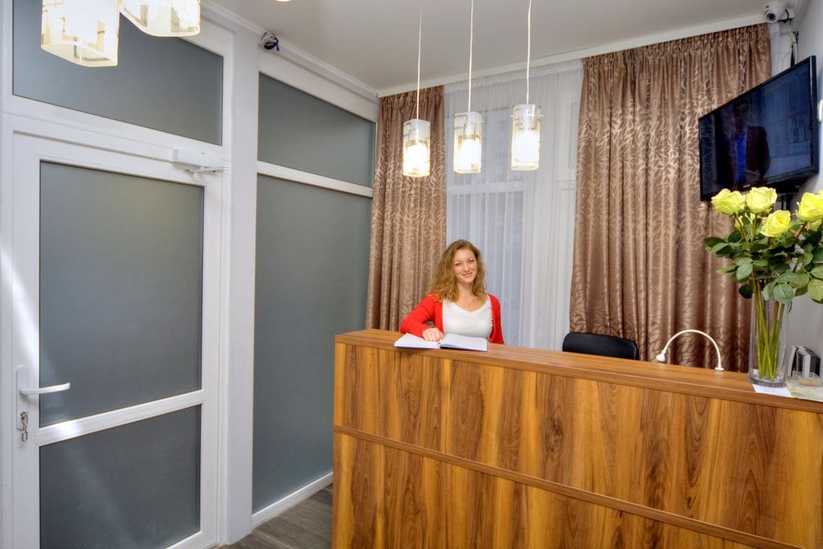 Un espace d’accueil avec un bureau en bois, un téléviseur fixé au mur et un vase rempli de fleurs jaunes.
