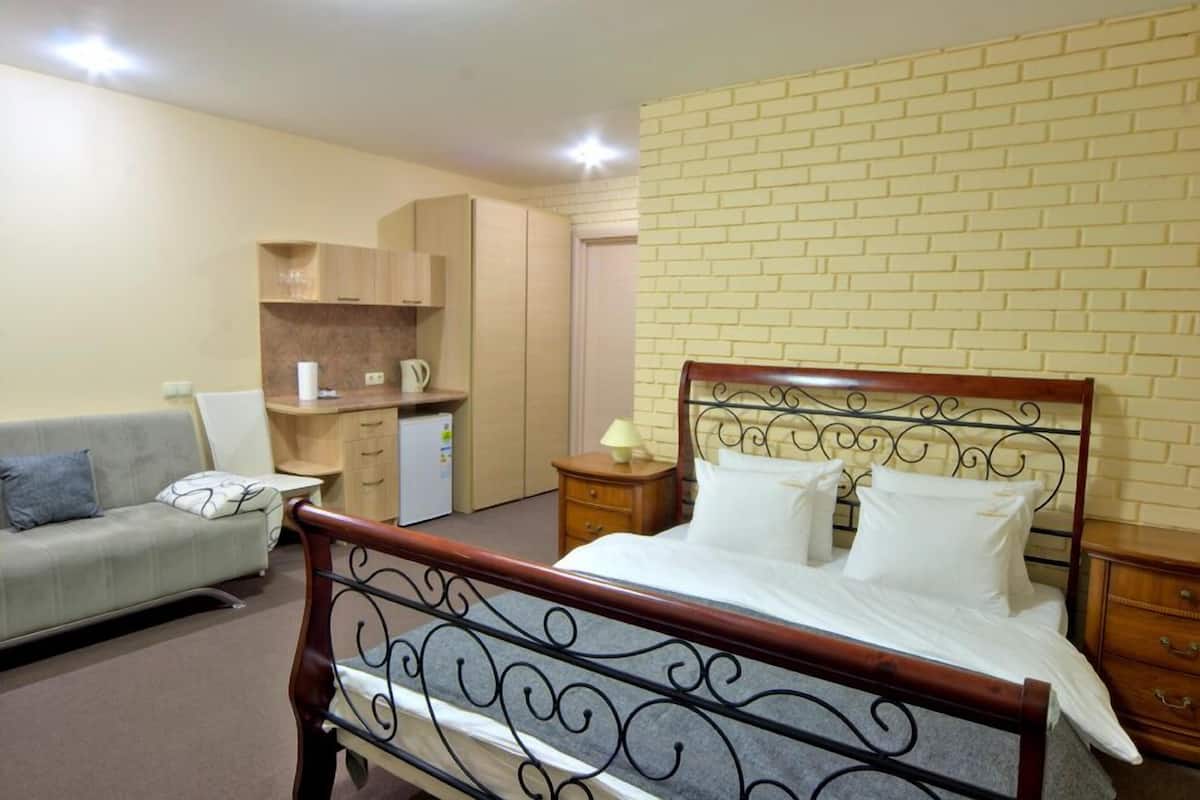 A bedroom with a wooden bed, a grey sofa, a small bedside table, a nightstand, and a wardrobe.