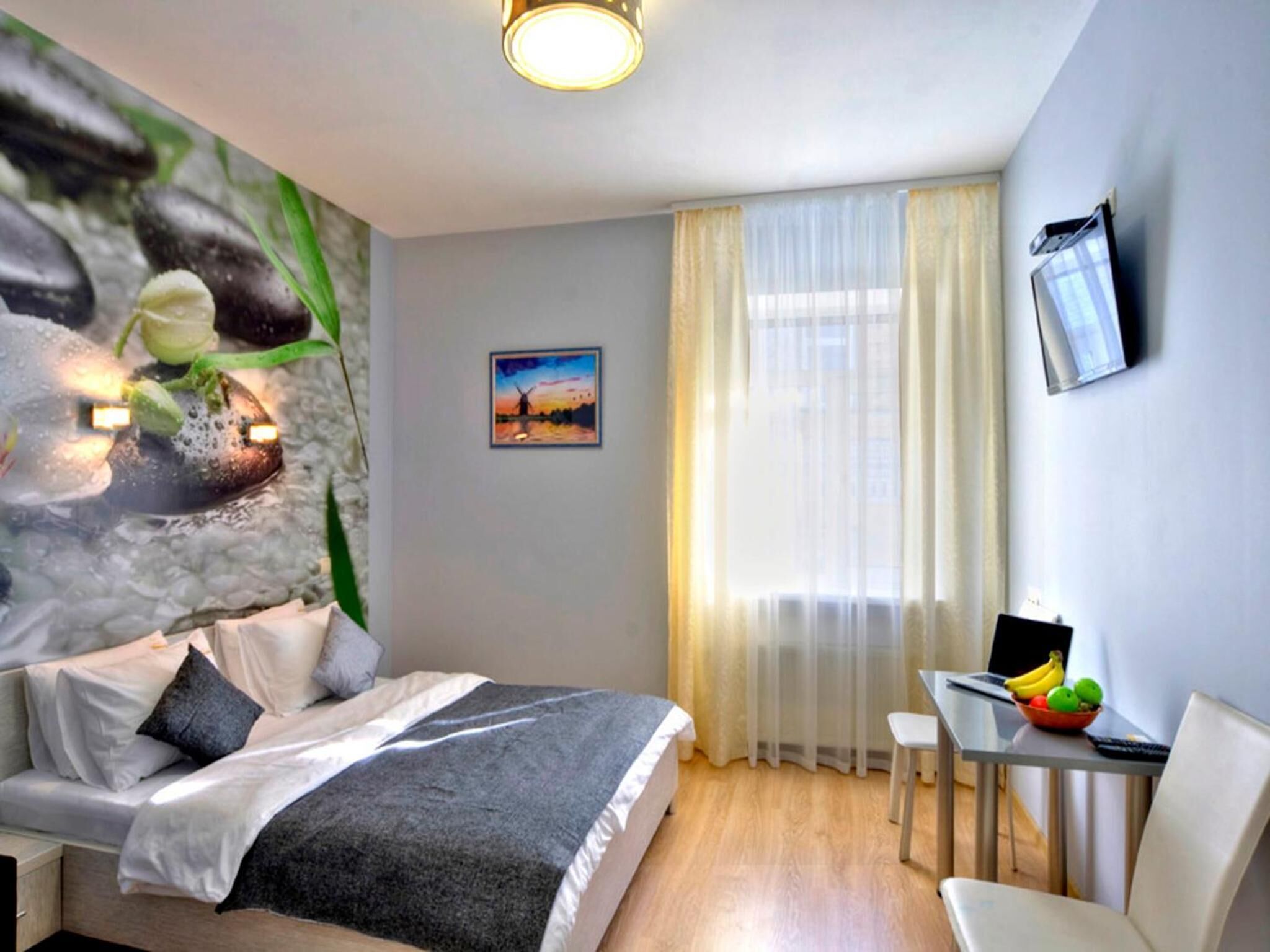 A hotel room with a bed, a desk with a chair, a television, and a painting on the wall.