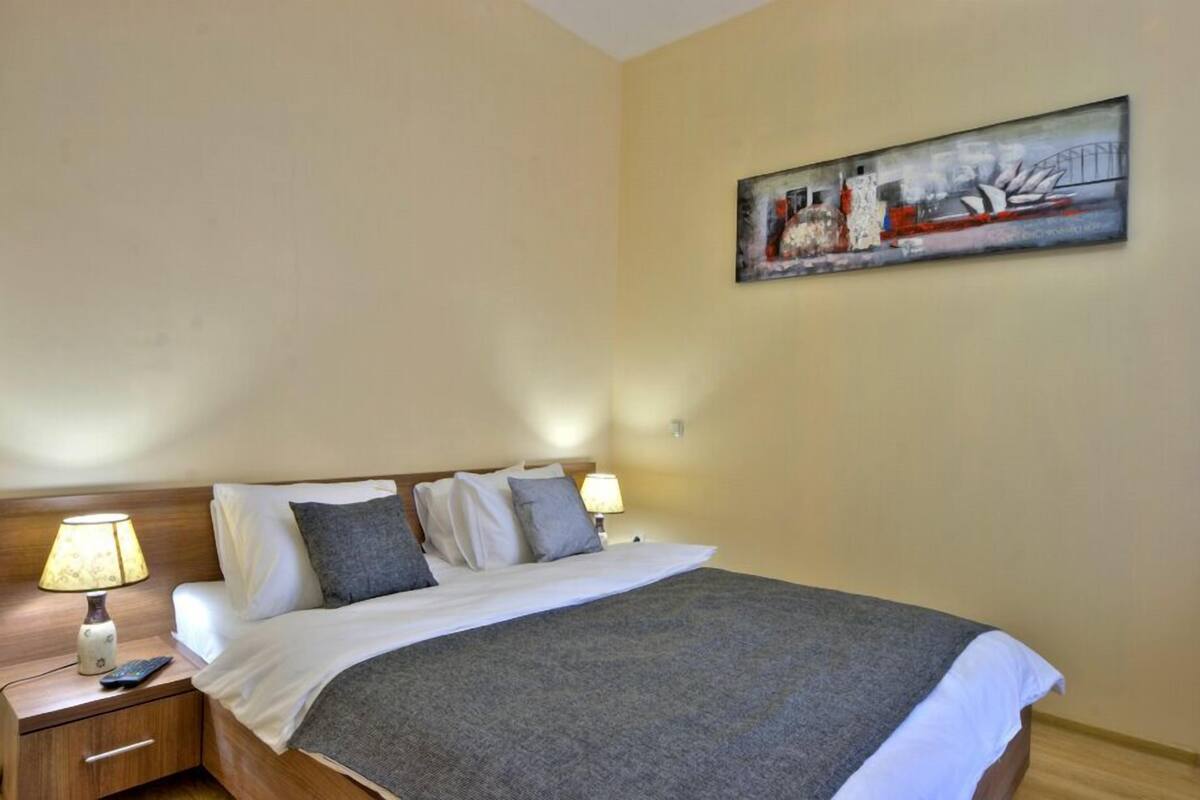 A hotel room with a bed, two bedside lamps, a nightstand, and a painting on the wall.