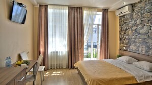 A hotel room with a bed, a desk with a chair, a TV mounted on the wall, and a stone wall. - Golden Gate Inn (Kyiv)