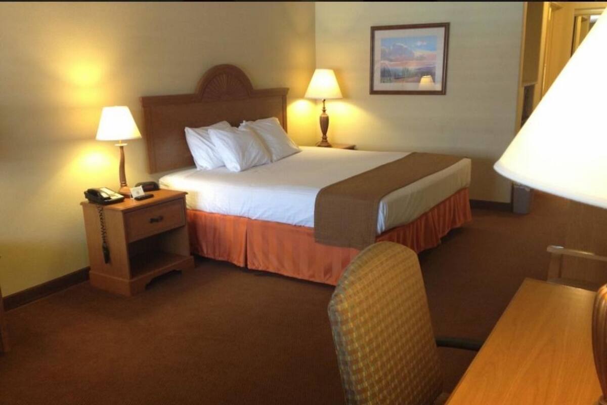 A hotel room with a bed, two bedside tables with lamps, a chair, and a desk.