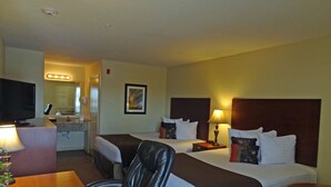 Quarto de hotel com duas camas, uma mesa de escritório com televisão, uma cadeira e uma mesinha.