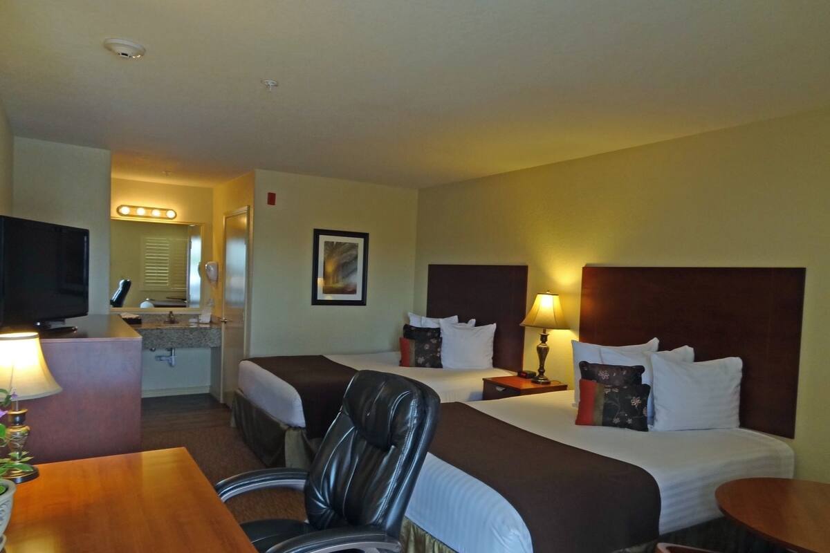 A hotel room with two beds, a desk with a TV, a chair, and a small table.