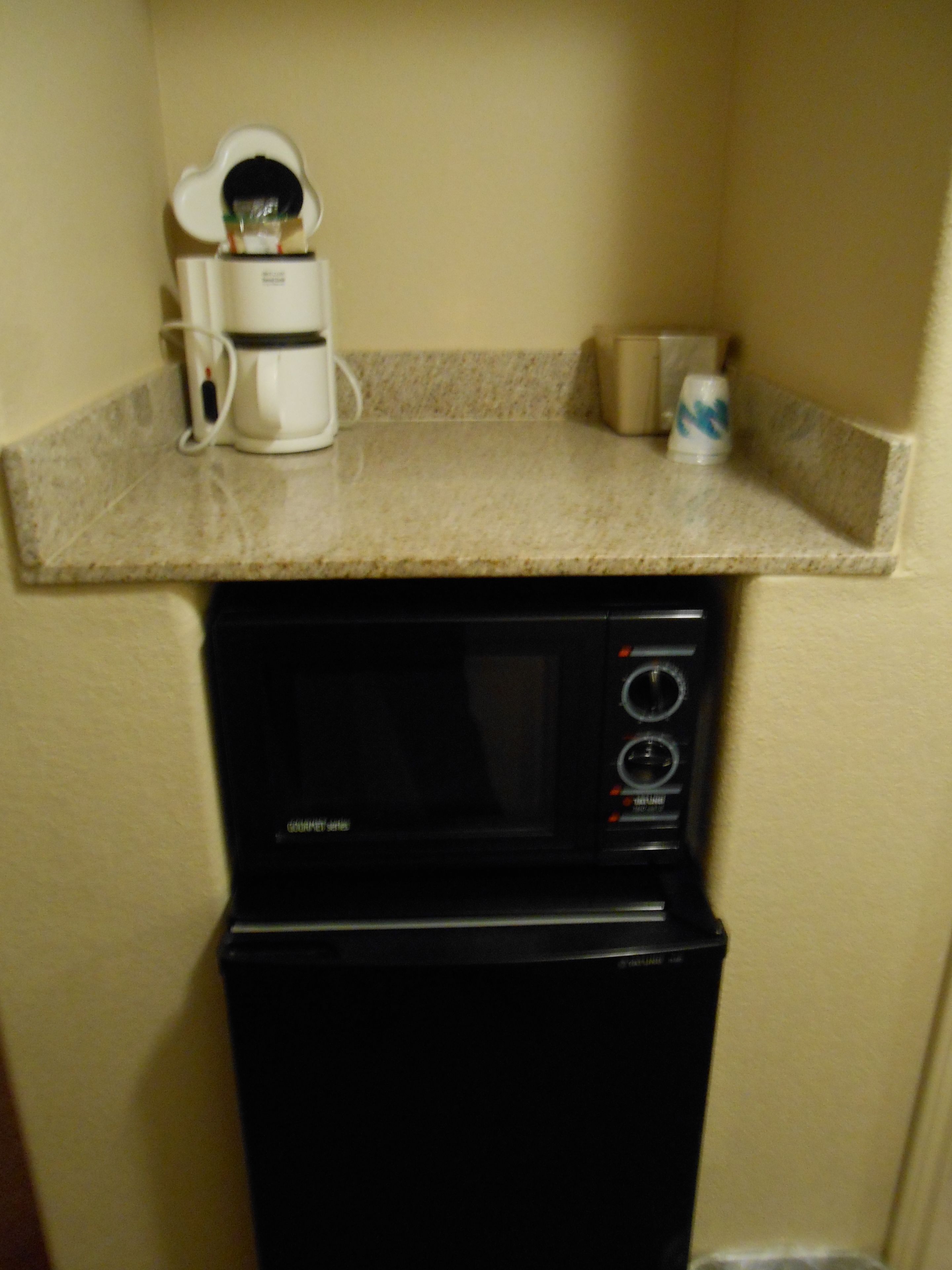 A kitchenette with a coffee maker, microwave, and a small countertop.