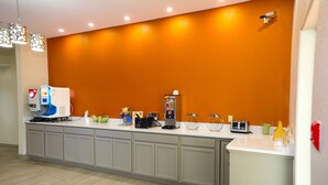 Uma área de recepção com balcão, dispensadores de água, máquina de café e um pequeno frigorífico.