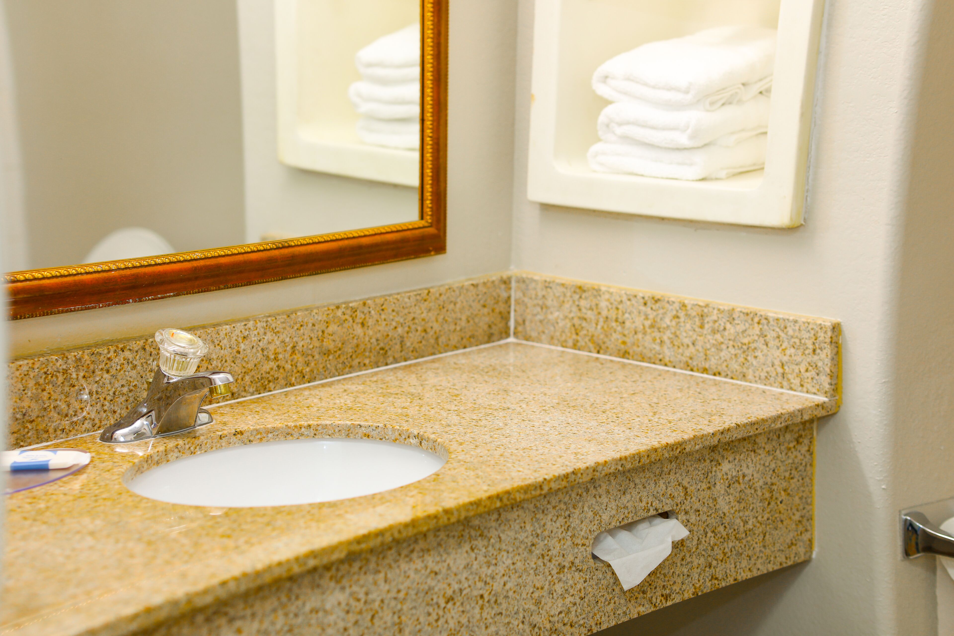 A bathroom sink with a speckled countertop, a mirror, and a towel rack with folded towels.