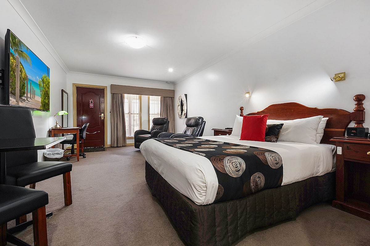 A hotel room with a large bed, a desk with a chair, a TV, and a door leading to another room.