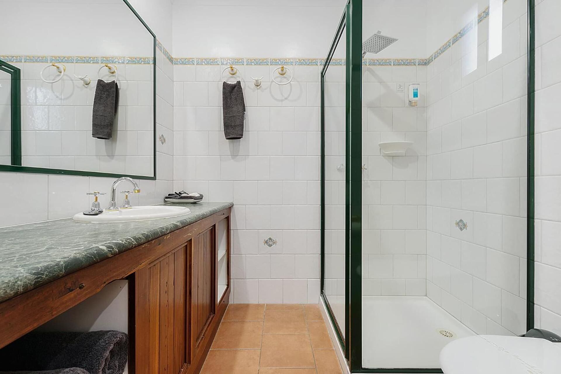 Een badkamer met een marmeren wastafel, houten kasten, een glazen douchecabine en een toilet.