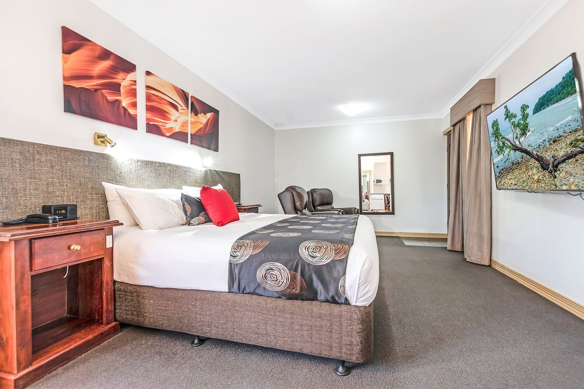 A hotel room with a large bed, a desk, a chair, and artwork on the walls.