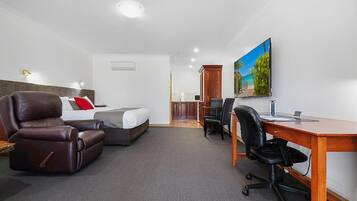 Habitación de hotel con cama, escritorio, dos sillas, televisor y un cuadro en la pared.