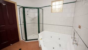 A bathroom with a glass shower enclosure, a white bathtub, and a door.