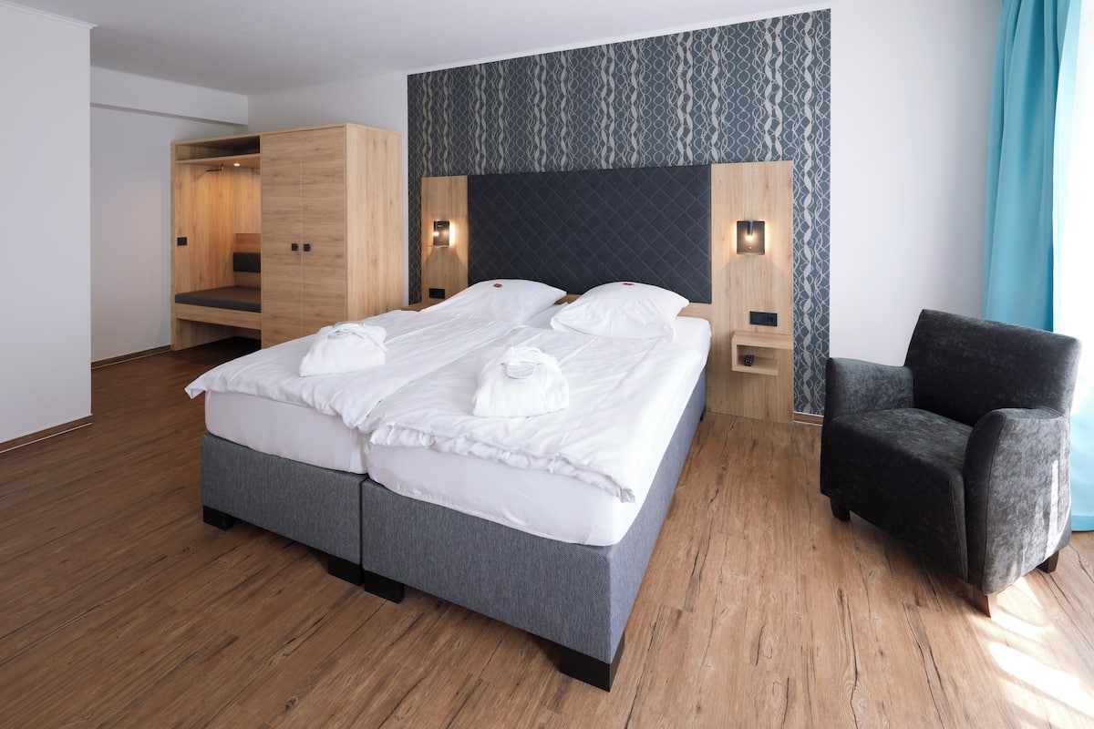 A modern hotel room with a large bed, a wardrobe, a chair, and a patterned wall.