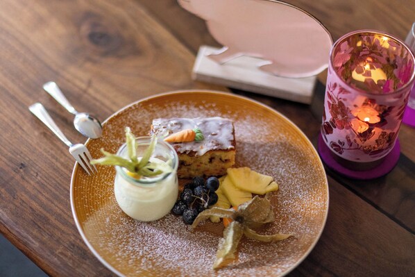 A dessert plate with a slice of cake, blueberries, a dollop of cream, and a sprig of mint on a wooden table.