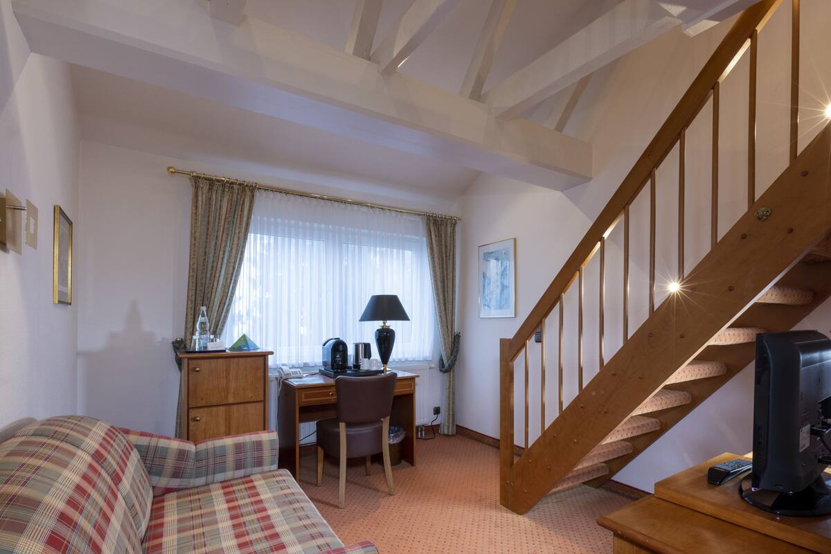 A hotel room with a bed, a desk, a chair, a television, and a staircase.