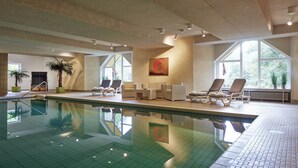 Une piscine intérieure dotée de chaises longues et d’une grande fenêtre.