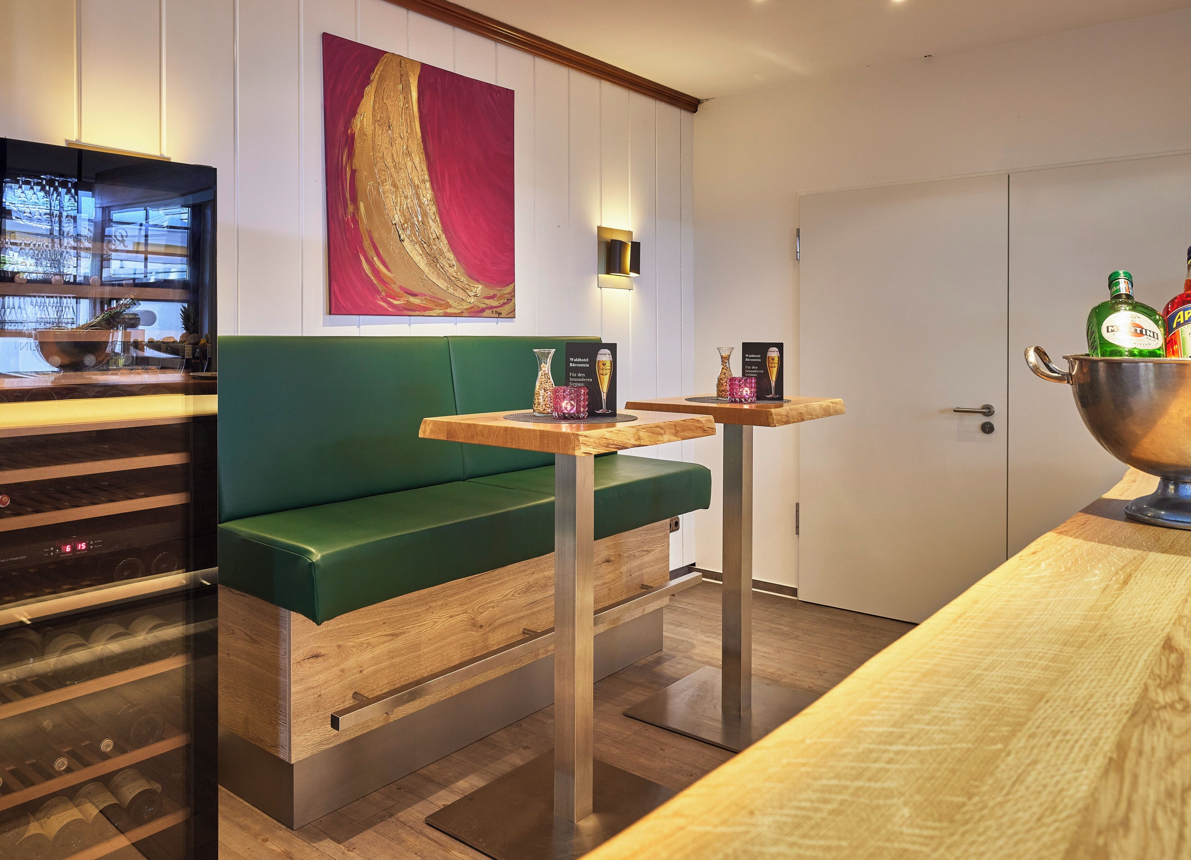 Una habitación de hotel moderna con un sofá verde, una mesa de madera y un minibar.