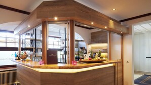 Un espace d’accueil d’hôtel avec un comptoir de réception en bois, des étagères en verre pour exposer des objets et un panier de fruits.