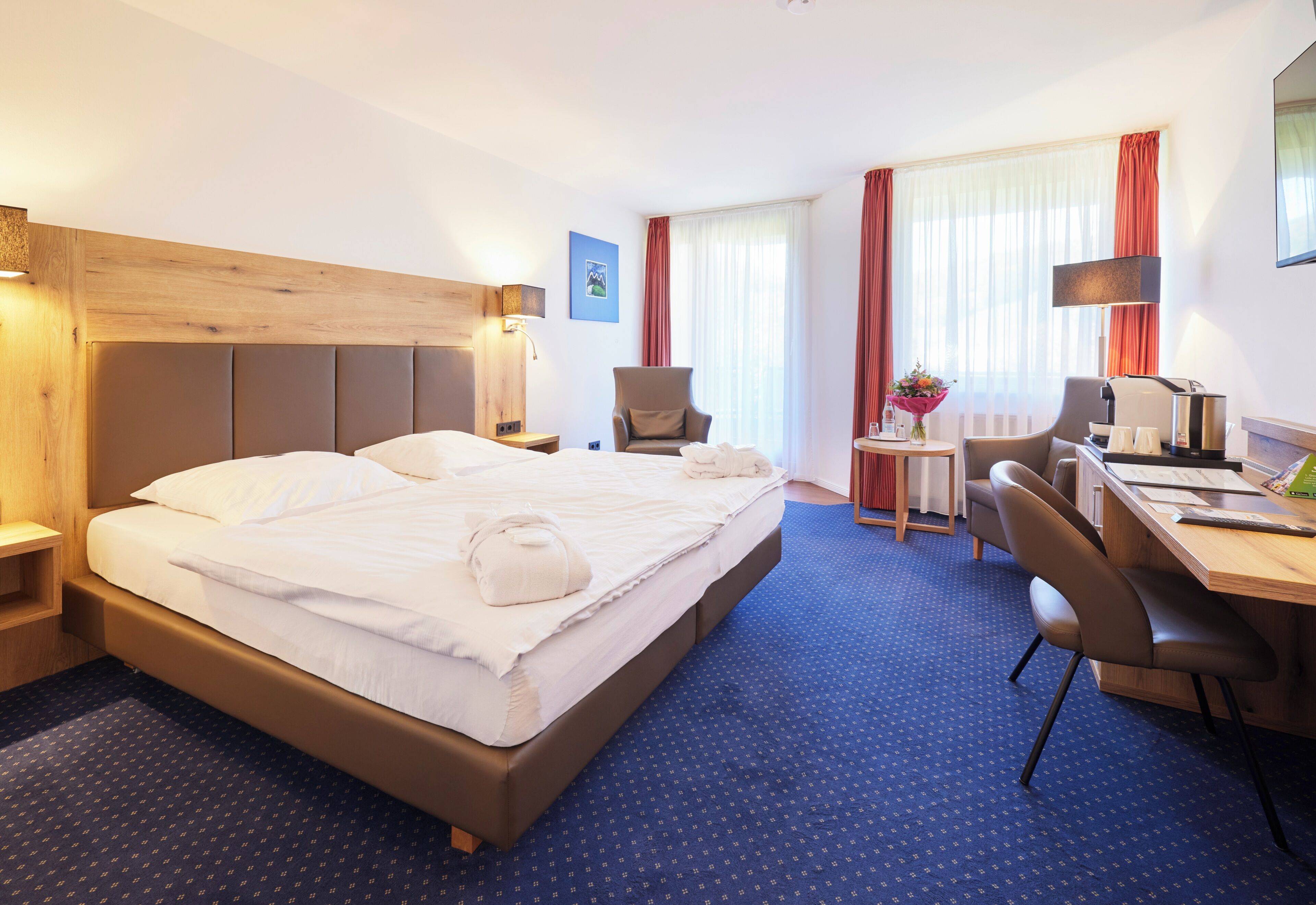 Ein Hotelzimmer mit einem großen Bett, einem Schreibtisch, einem Stuhl und einem kleinen Tisch.