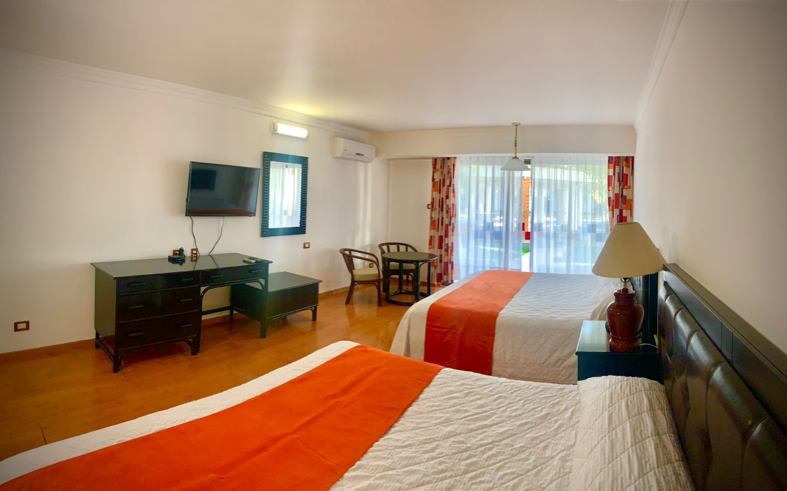 Habitación de hotel con dos camas, un escritorio, una silla, un televisor y una ventana con cortinas.