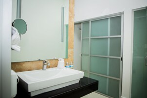 Un baño con lavamanos blanco, un espejo, dispensador de toallas y cabina de ducha de vidrio.