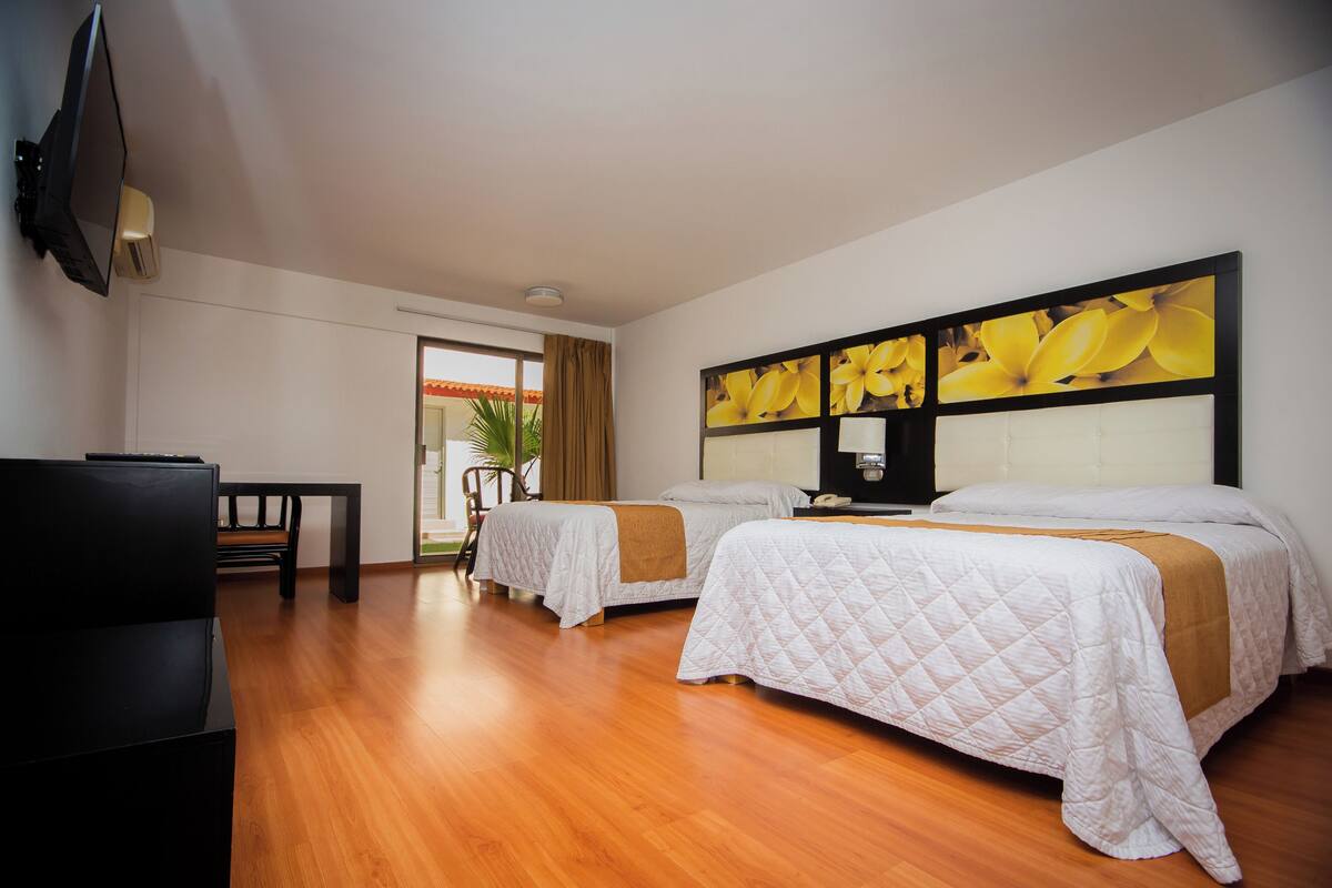 A hotel room with two beds, a TV, and a wooden floor.