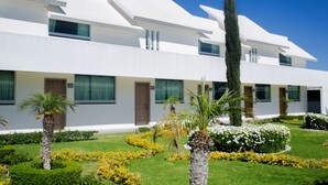 A modern building with a flat roof, multiple windows, and a well-maintained garden with palm trees and flowers.