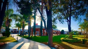 A pathway leading to a building with a red roof and white walls, surrounded by trees and well-maintained grass.