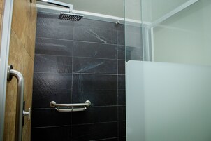 A bathroom with black tiles, a glass shower enclosure, and a metal grab bar.