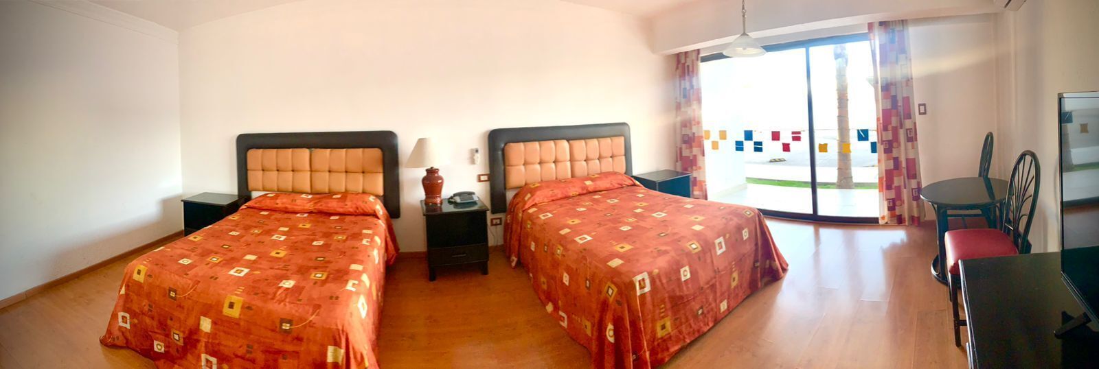 Habitación de hotel con dos camas, una mesita, una silla y vistas al exterior.