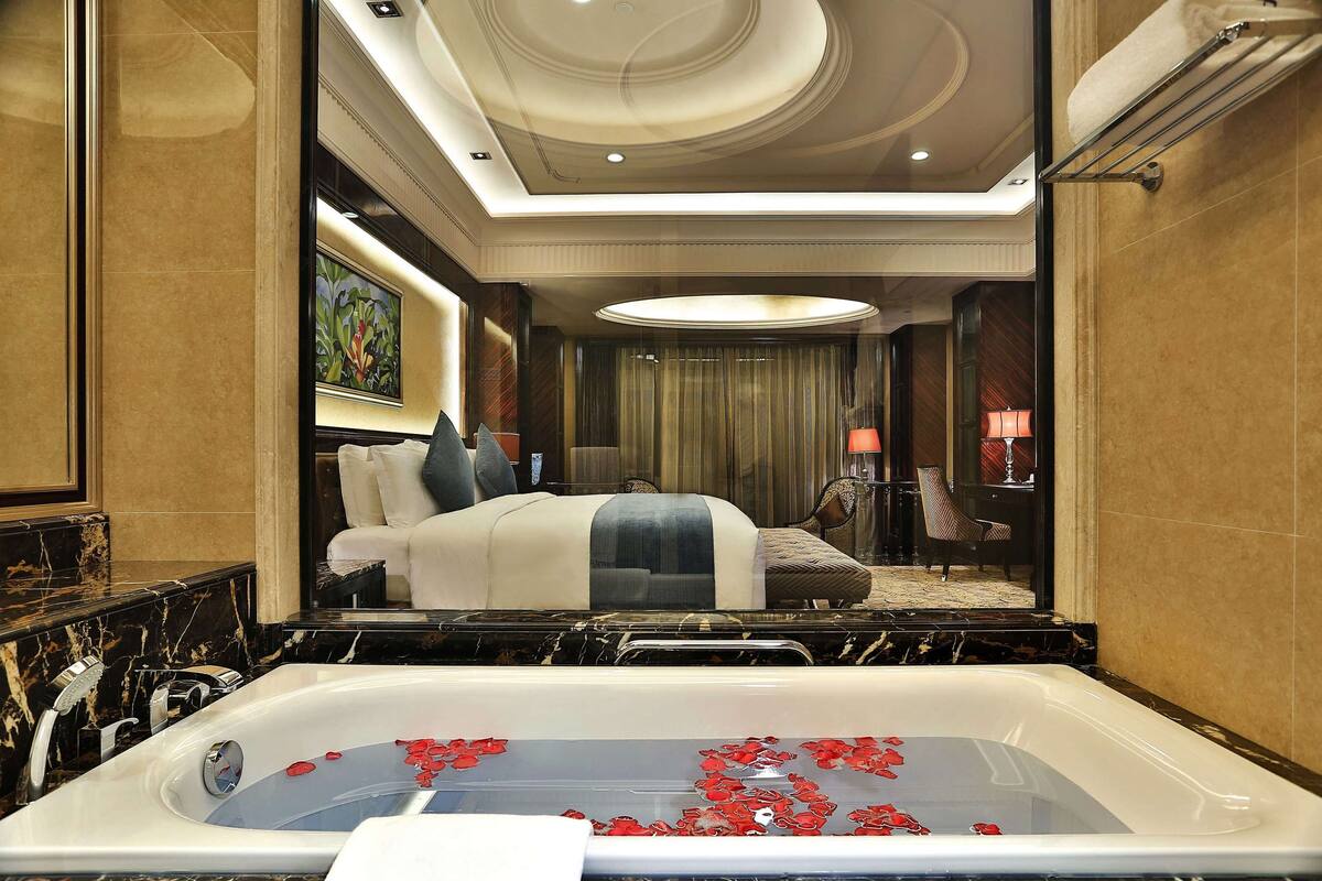 A luxurious hotel room with a large bed, a sitting area, and a bathtub with rose petals.