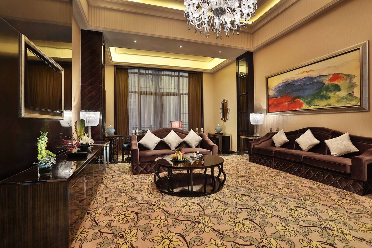 A hotel lobby with a large chandelier, a sofa set, a round coffee table, and a large abstract painting on the wall.