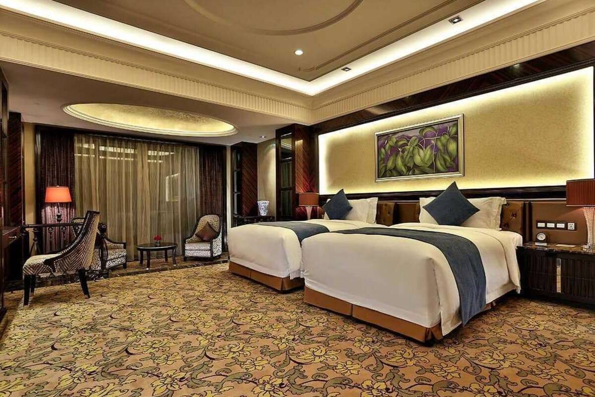 A hotel room with two beds, a desk, a chair, and a large painting on the wall.