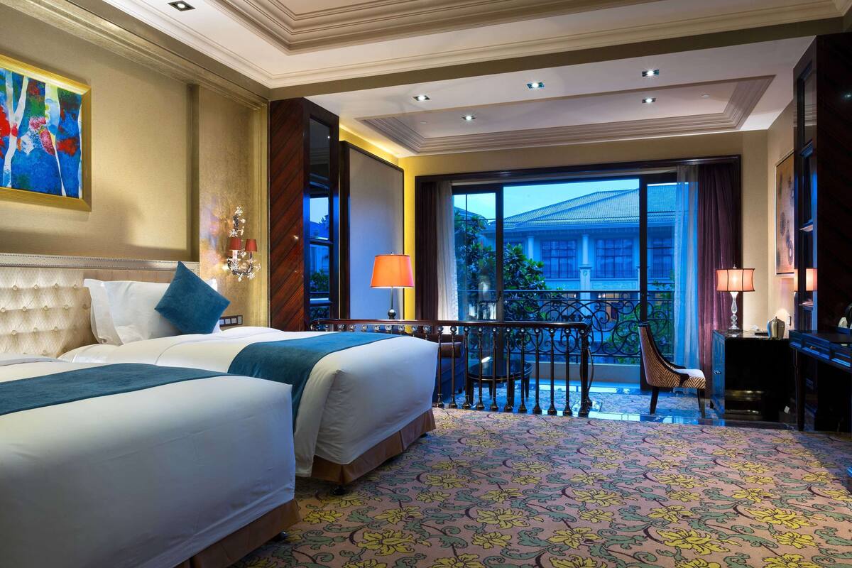 A hotel room with two beds, a balcony with a view, and a chandelier.