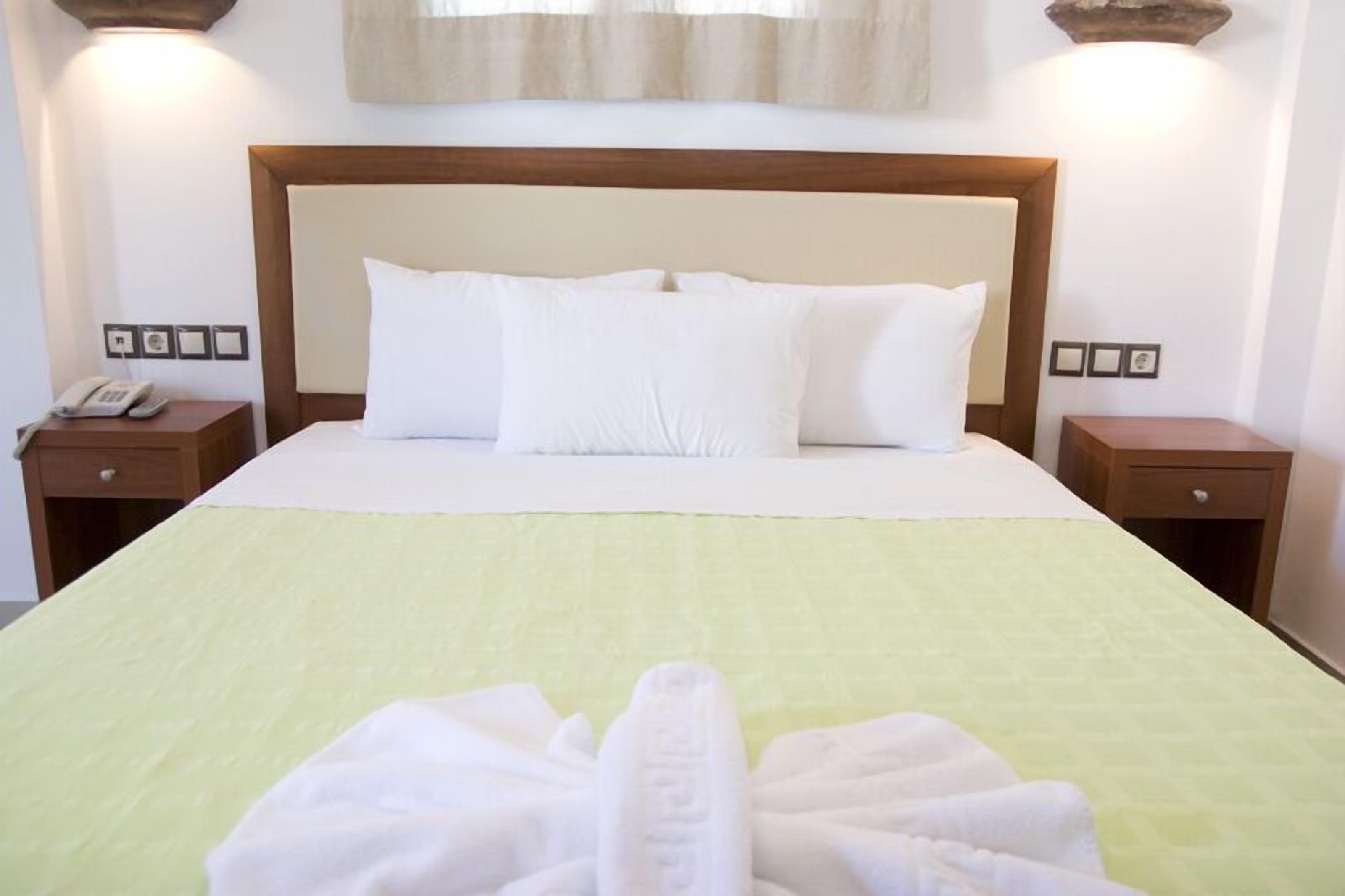 A neatly made bed with white linens and a green bedspread, two bedside tables with lamps, and a telephone on one of the tables.