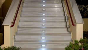 Eine Treppe mit Handlauf, einer Wandleuchte und Blumentöpfen am Fuß.