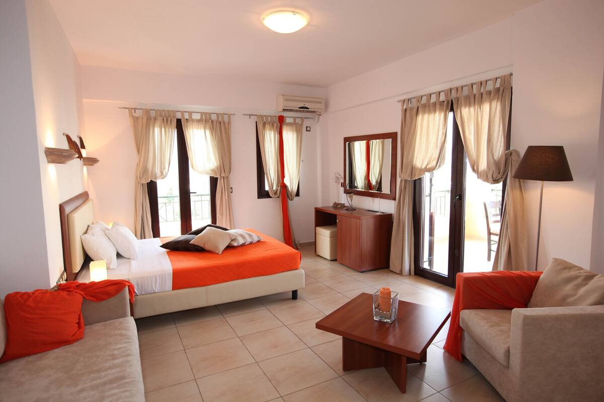 A hotel room with a bed, two sofas, a coffee table, a desk, and a mirror.