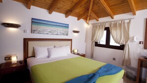 Ein Hotelzimmer mit Holzboden, einem Bett mit weißer und grüner Bettwäsche, einem Strandbild und einem Fenster mit Vorh ängen.