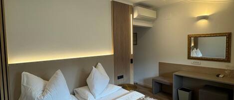 A hotel room with a large bed, a desk, a mirror, and an air conditioning unit.